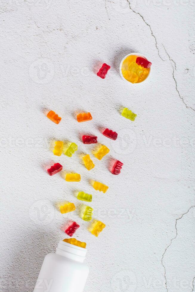 Bottle with gummy vitamin supplements in the shape of bears on the table top and vertical view photo