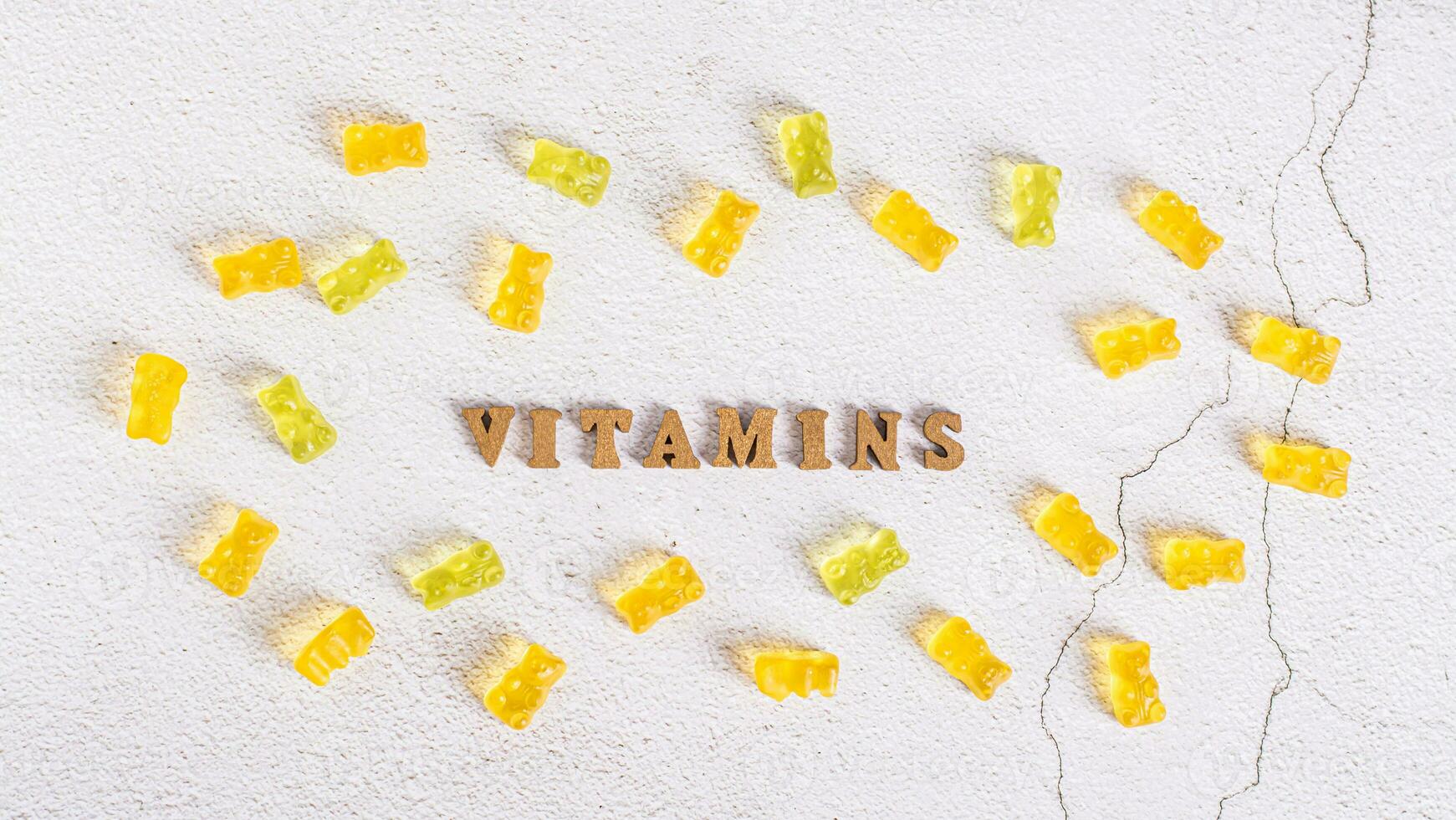 The word vitamins from letters and gummy vitamins in the form of candy bears around top view photo