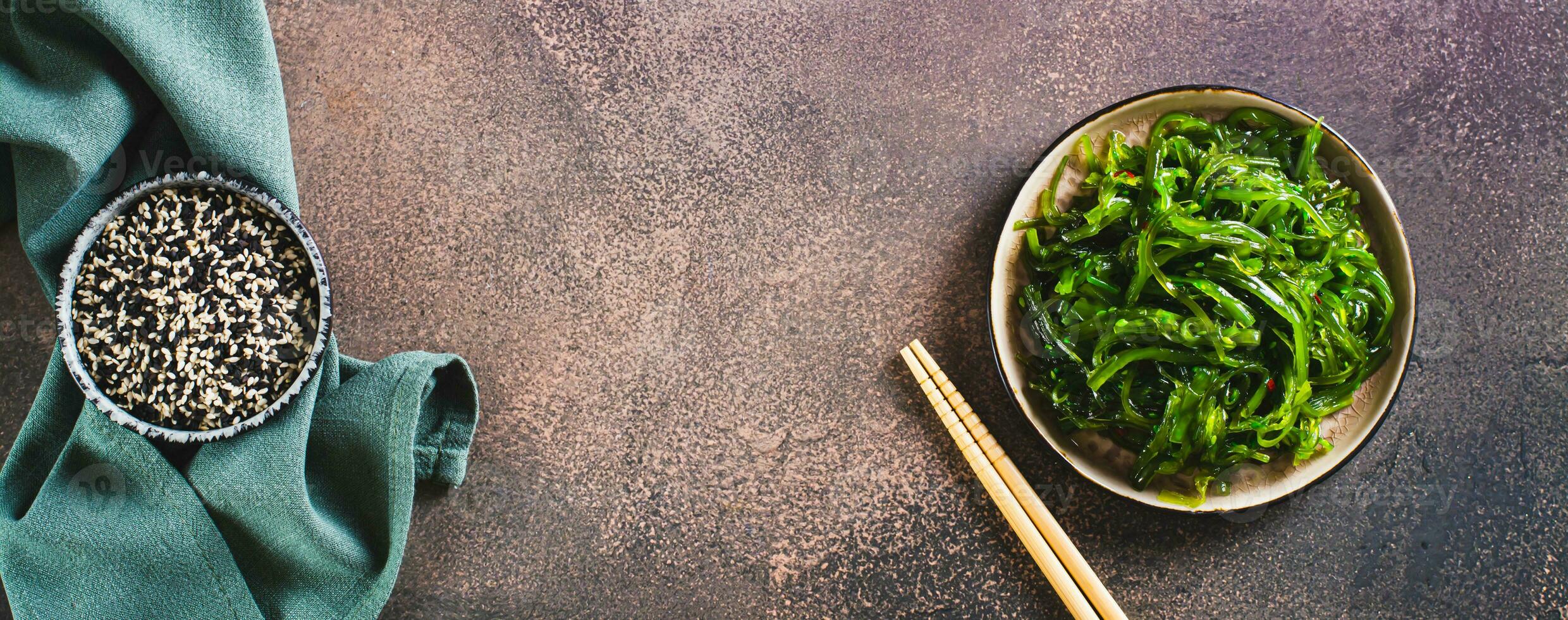 Delicious wakame seaweed salad on a plate and sesame seeds in a bowl top view web banner photo