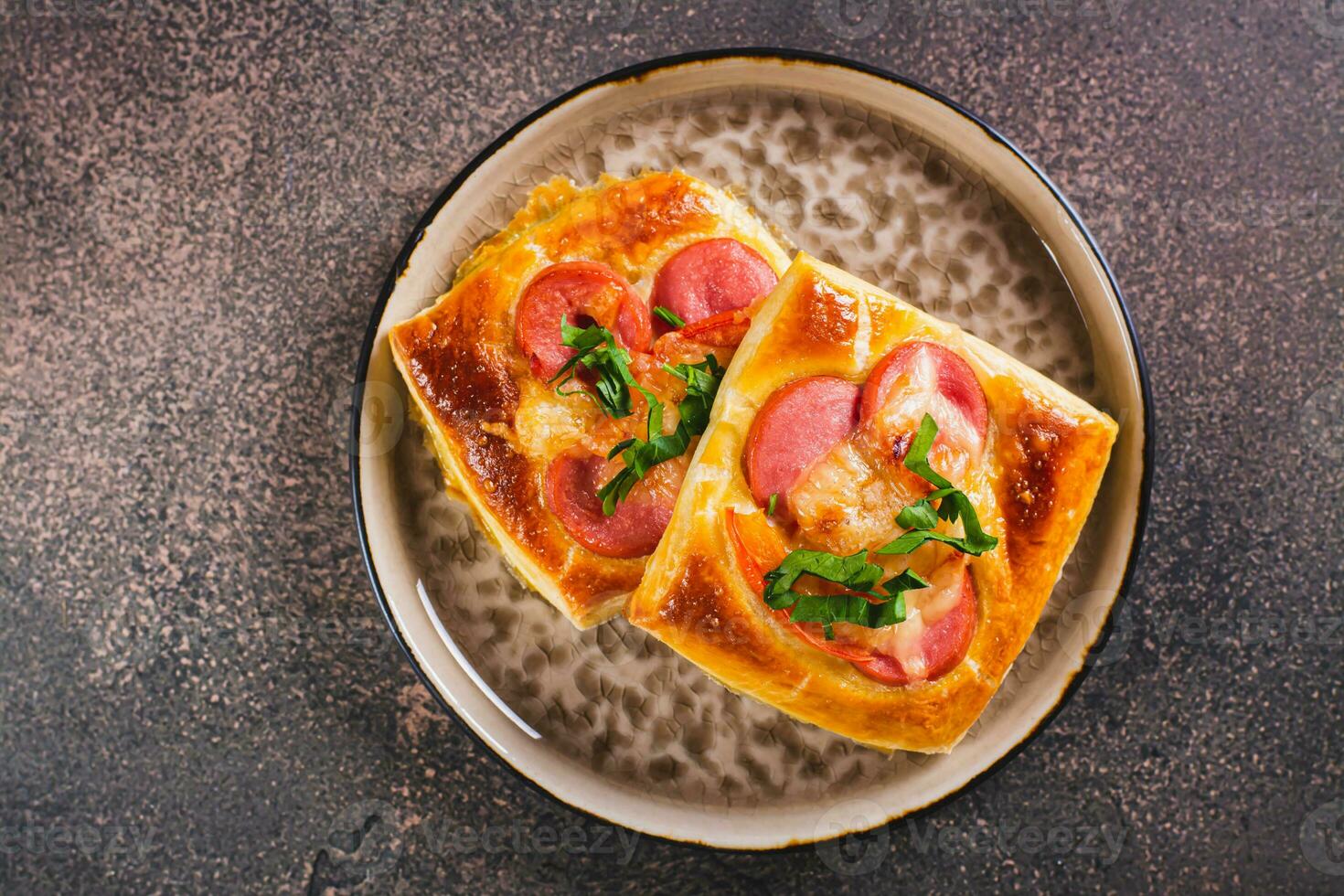 Close up of square mini pizza with tomato, sausage and cheese on a plate for a snack top view photo