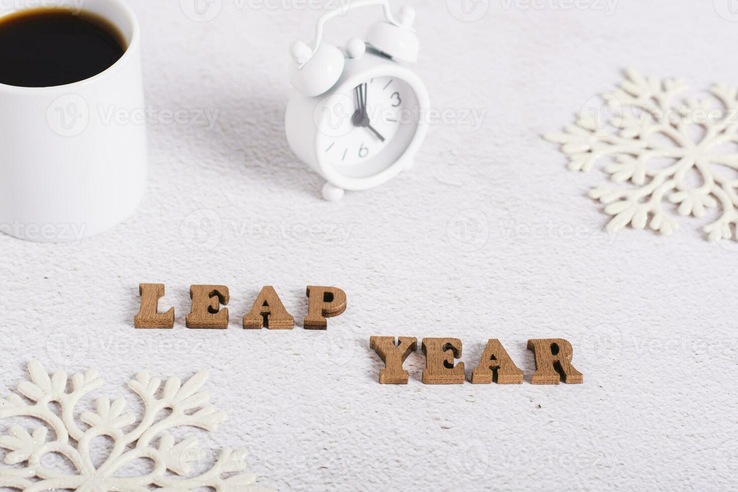 Leap year concept, text from wooden letters, alarm clock, coffee and snowflakes on light photo