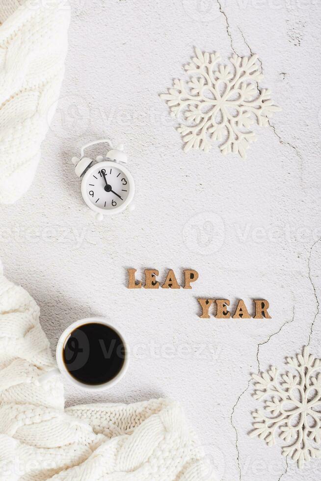 Leap year concept, coffee, alarm clock, snowflakes and letters on a light top and vertical view photo