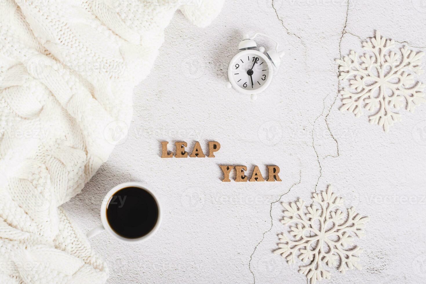 Leap year concept, coffee, alarm clock, snowflakes and letters on a light background top view photo