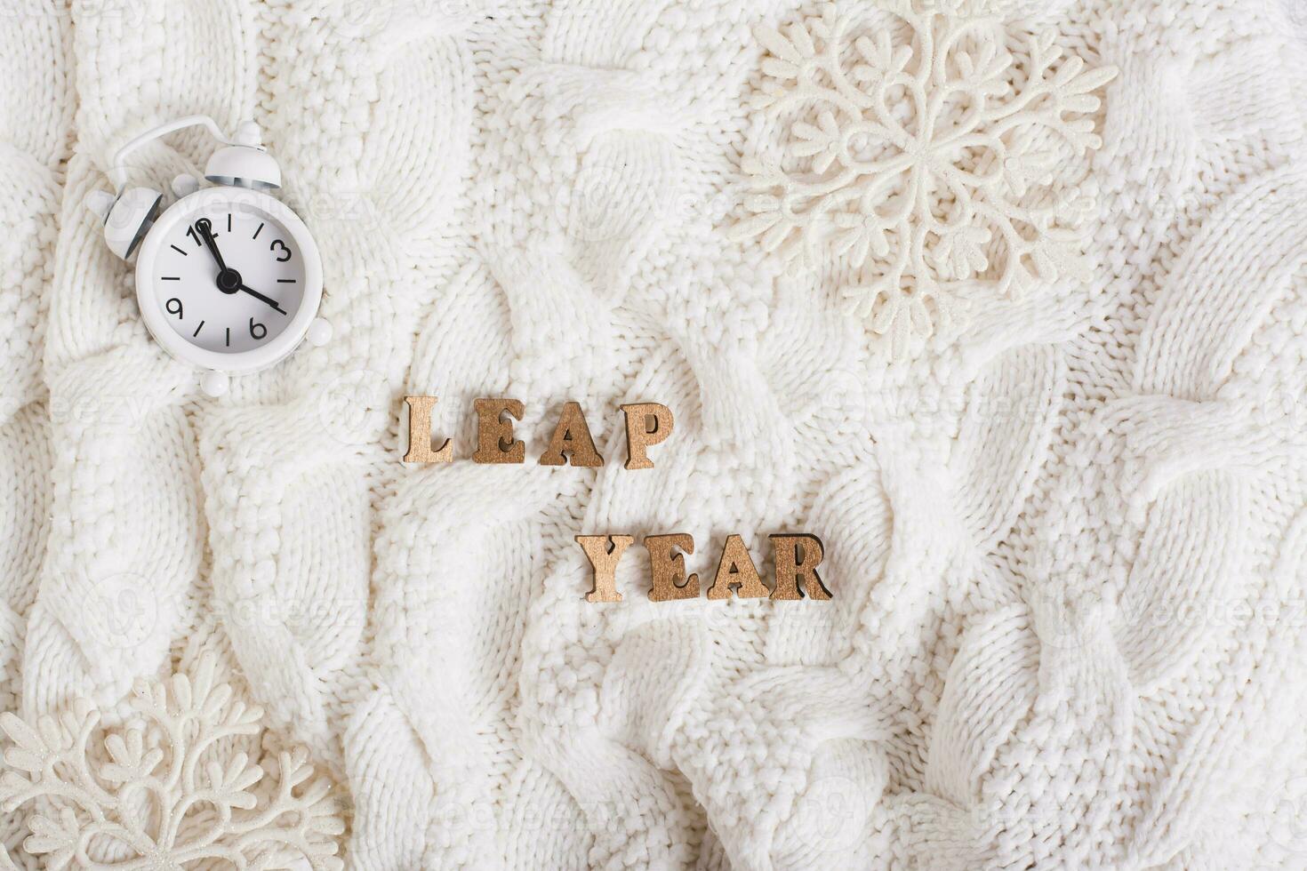 Leap year concept, text made of wooden letters, alarm clock and snowflakes on a knitted background photo