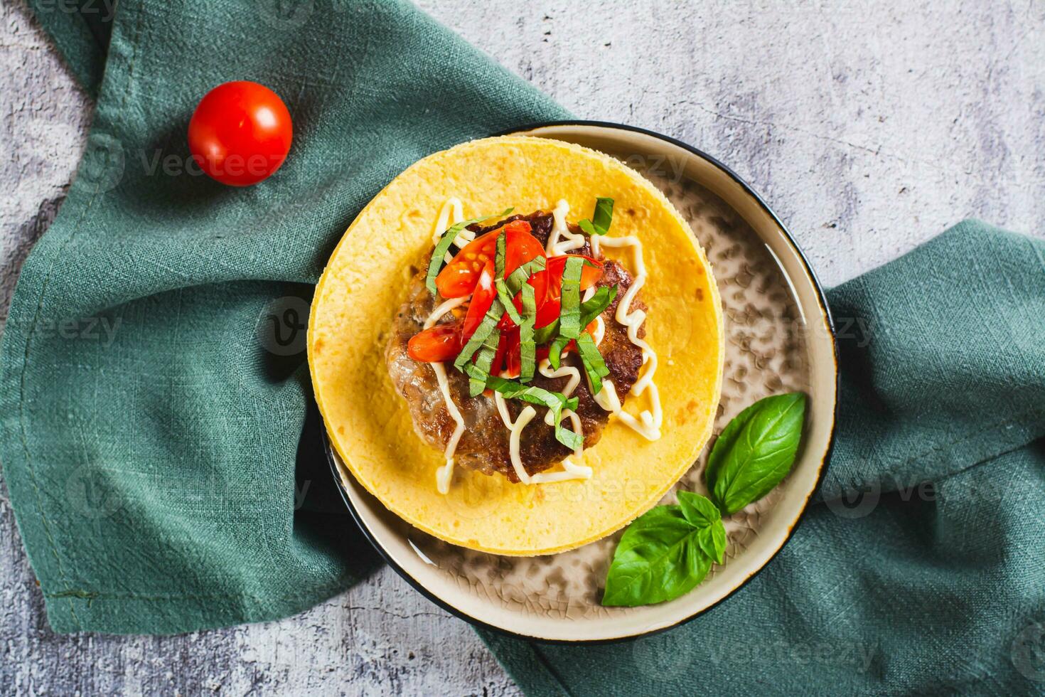 Close up of Smash Burger Tacos with beef patty, tomatoes and herbs on a plate top view photo