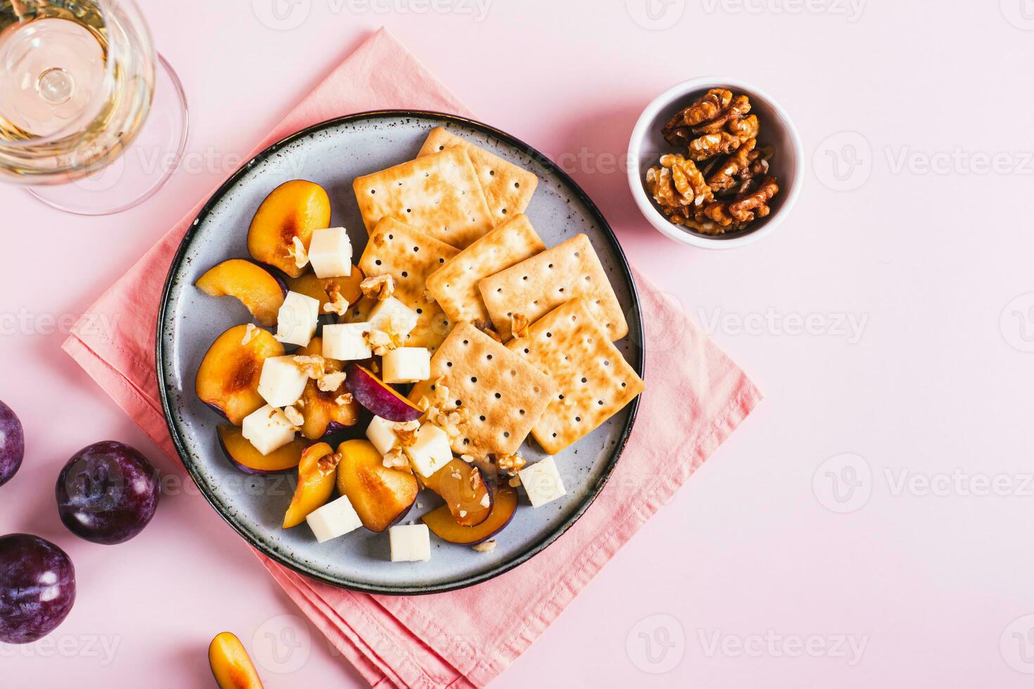 cena para chicas, queso, galletas, ciruelas en un plato y un vaso de vino en el mesa parte superior ver foto