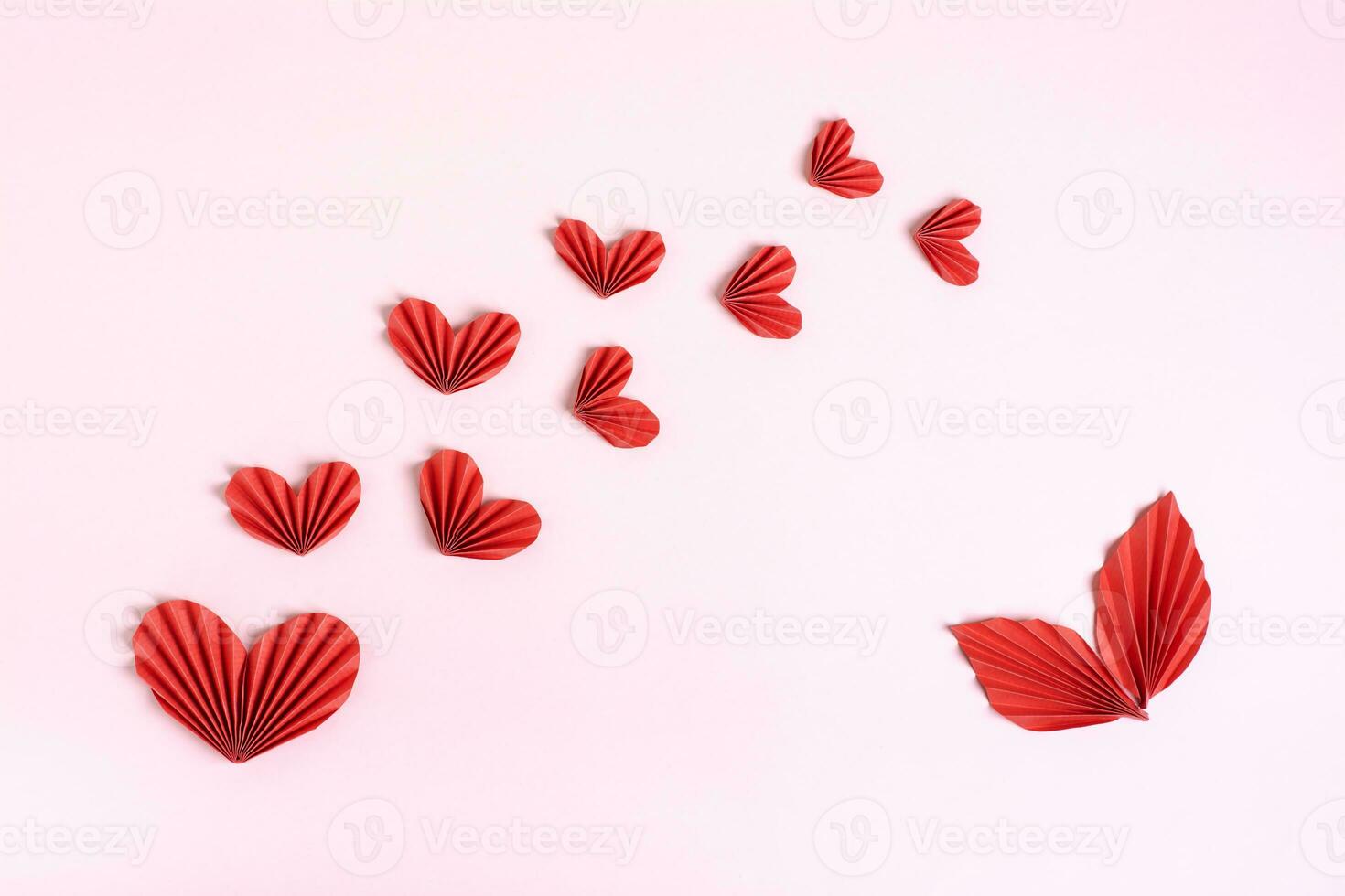 Composition of folded red paper hearts and leaves on a pink background top view photo