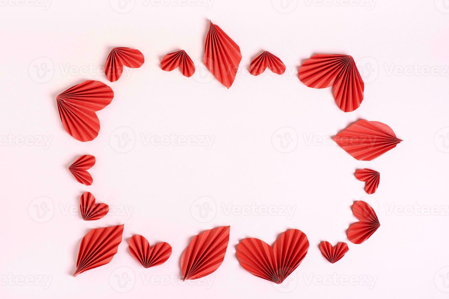 Frame of folded red paper hearts and leaves on pink background top view photo