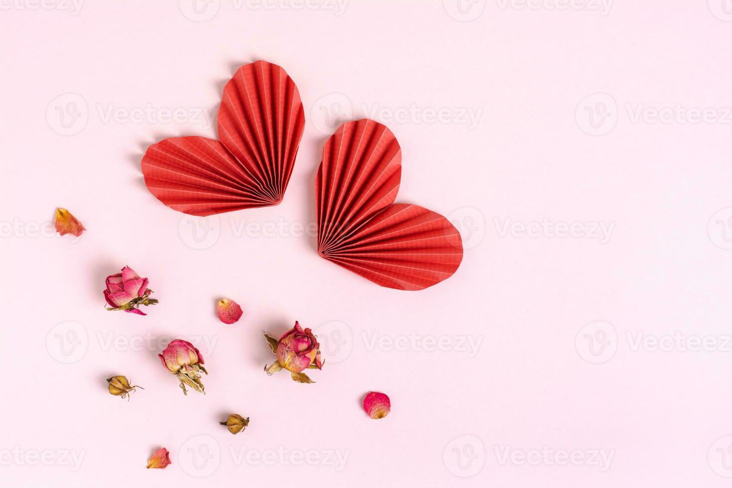 Pair of folded red paper hearts and wilting flowers on pink background photo