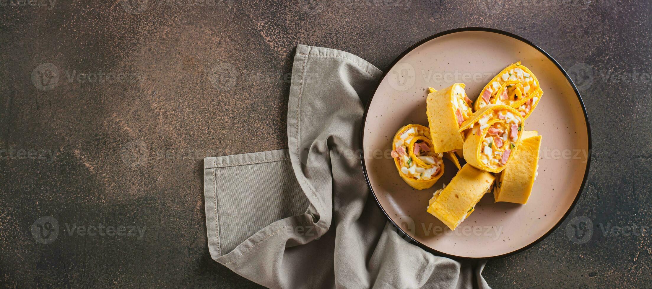 Tortilla rolls with salad of sausages, eggs, cheese and herbs on a plate top view web banner photo