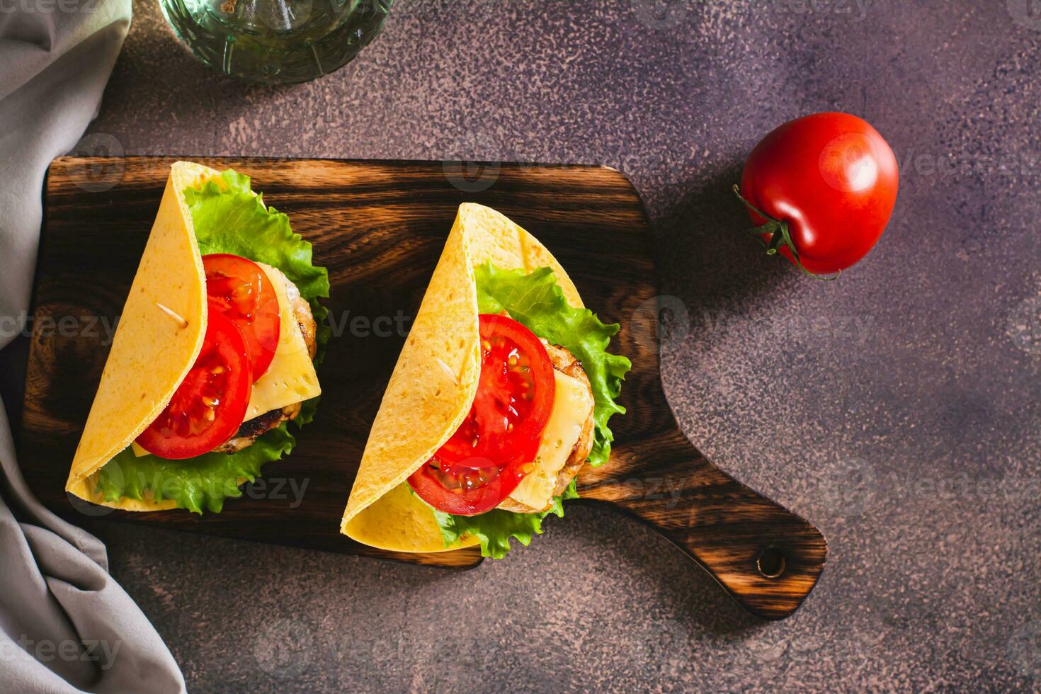 Taco burger with cutlet, cheese and tomatoes on a board on the table top view photo