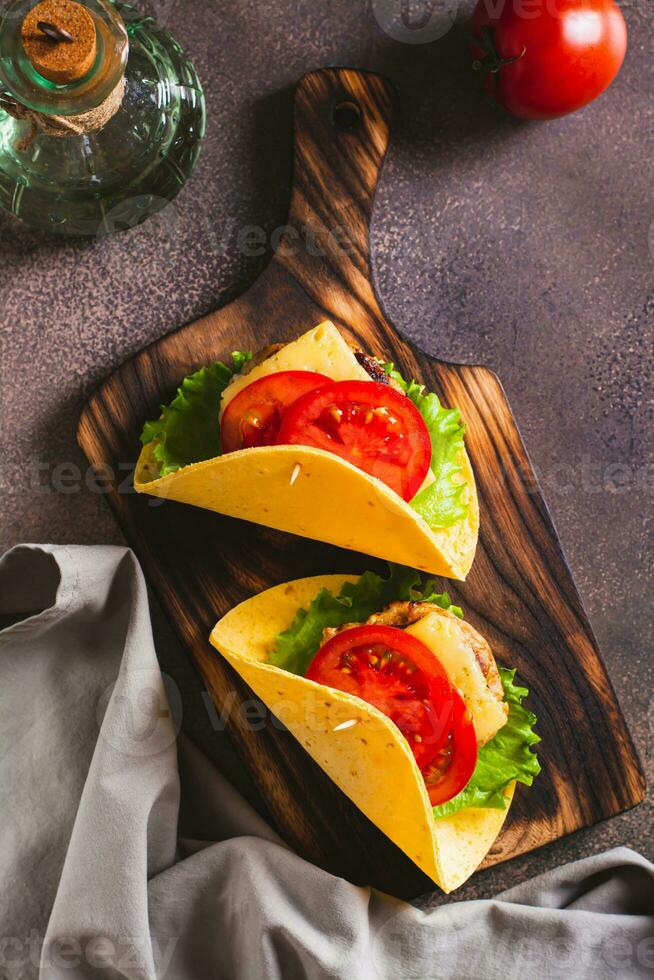 Taco burger in tortilla with cutlet, cheese and tomatoes on a board top and vertical view photo