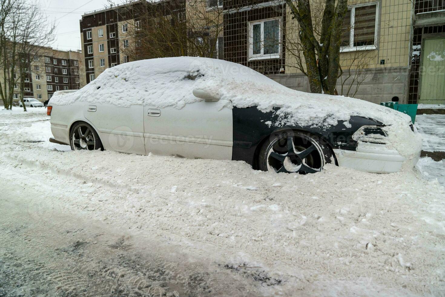 Snowy urban street with a car hidden under snow after snow removal photo