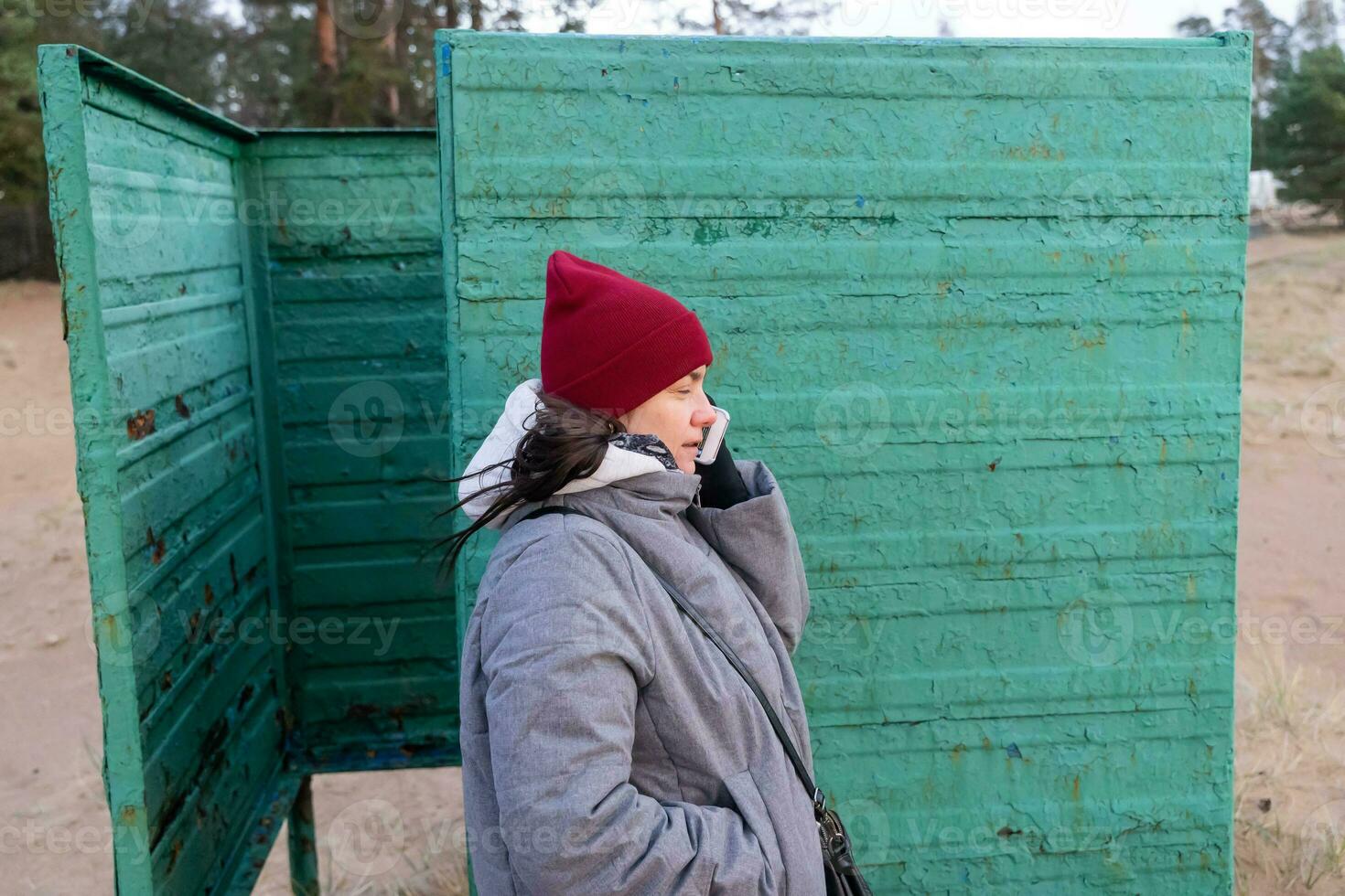 Portrait of Woman Wearing Autumn Clothes, Talking on Phone in Vintage Beach Changing Booth photo