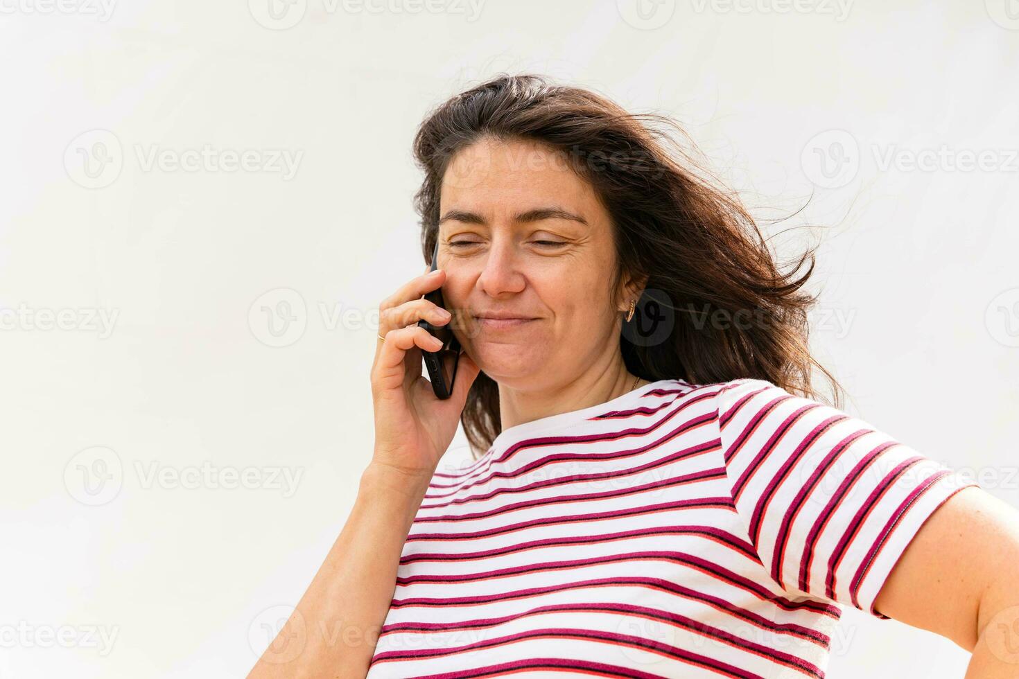 de pelo largo de edad mediana caucásico mujer en a rayas blusa alegremente utilizando móvil teléfono foto