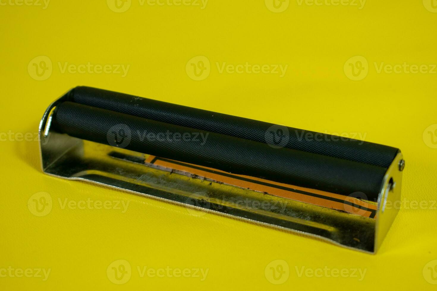 A black metal roller for make cigarette, cigarette roller handmade on yellow background photo