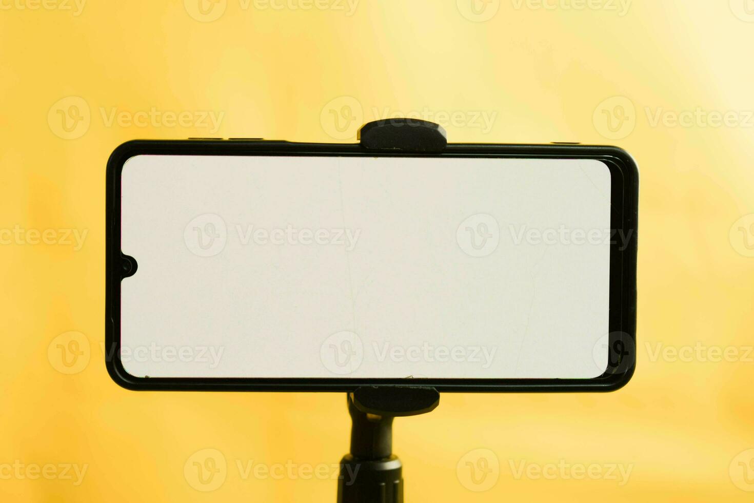 Landscape phone with white screen fixed to tripod on yellow background, for mockup design. photo