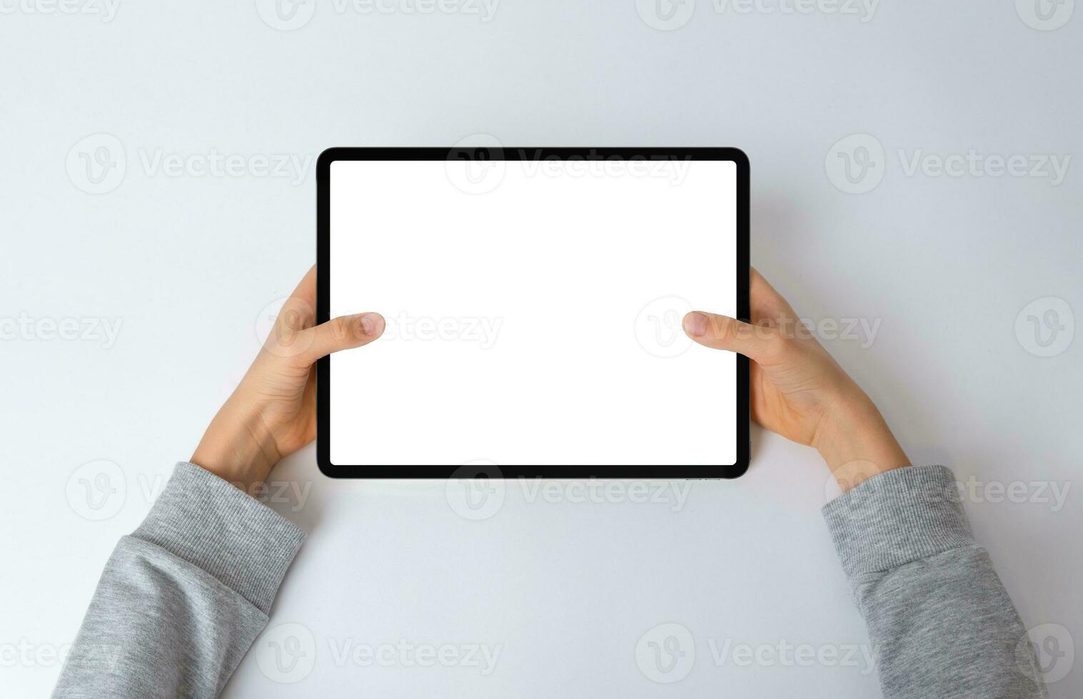 Top view of a kid's hands holding a horizontal tablet on a desk. Flat lay composition with an isolated screen for mockup, perfect for showcasing interactive content photo