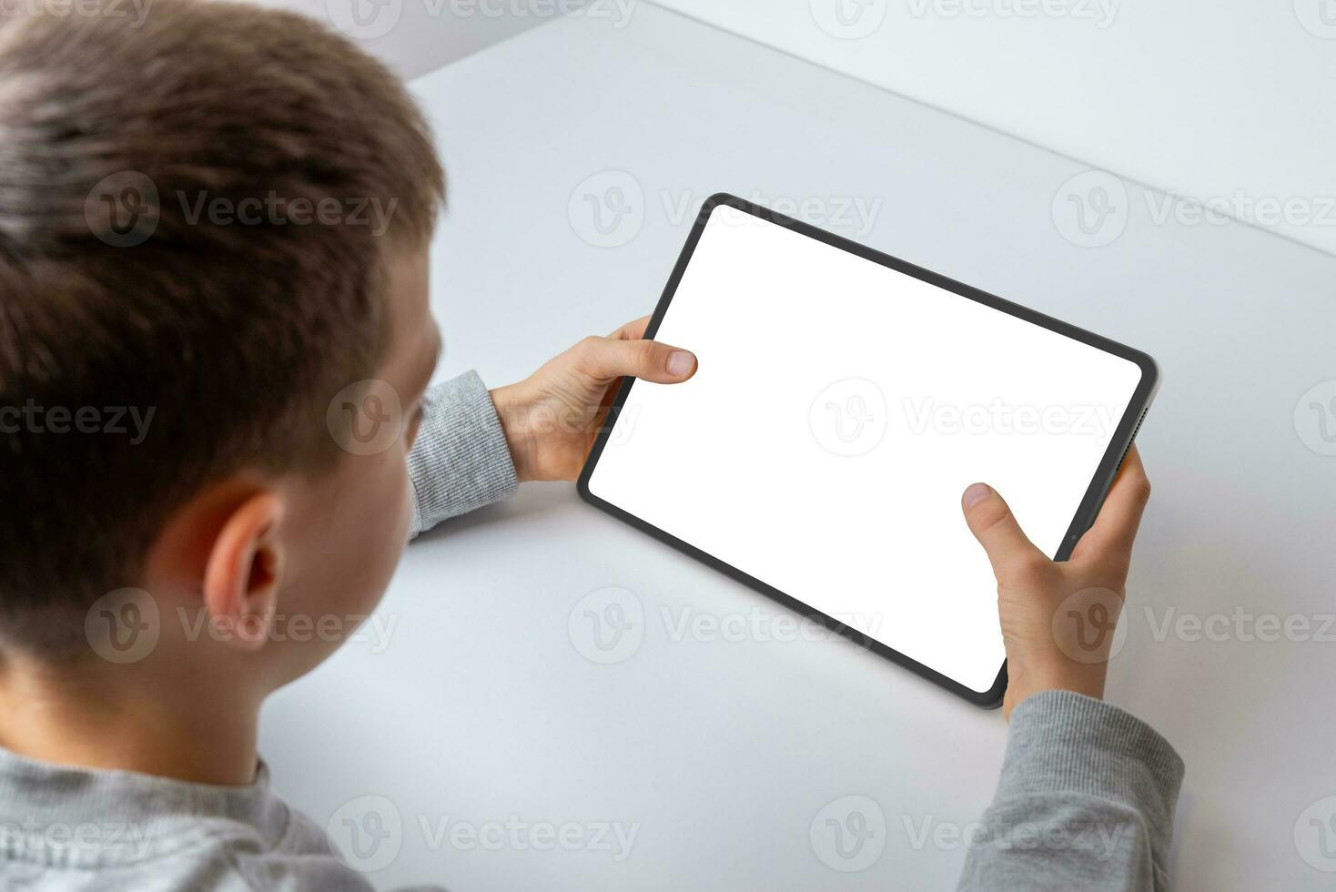 Boy at work desk, close-up view from behind, interacting with a tablet's isolated screen for game or app promotion. Engaged in digital entertainment photo