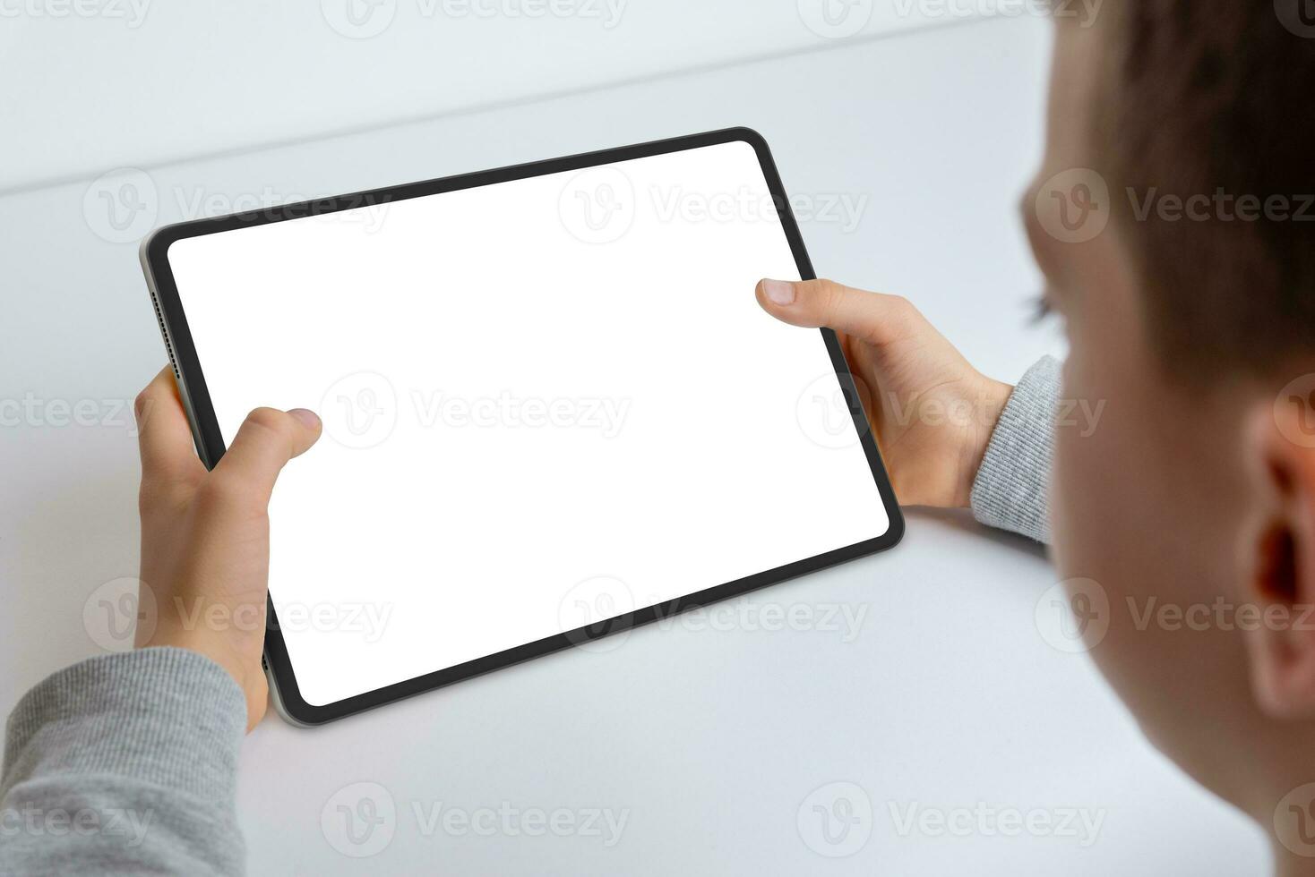 Close-up of a boy's hands holding a tablet mockup. Engaged in work, showcasing an isolated white screen for app presentation. Modern technology in kid hands photo