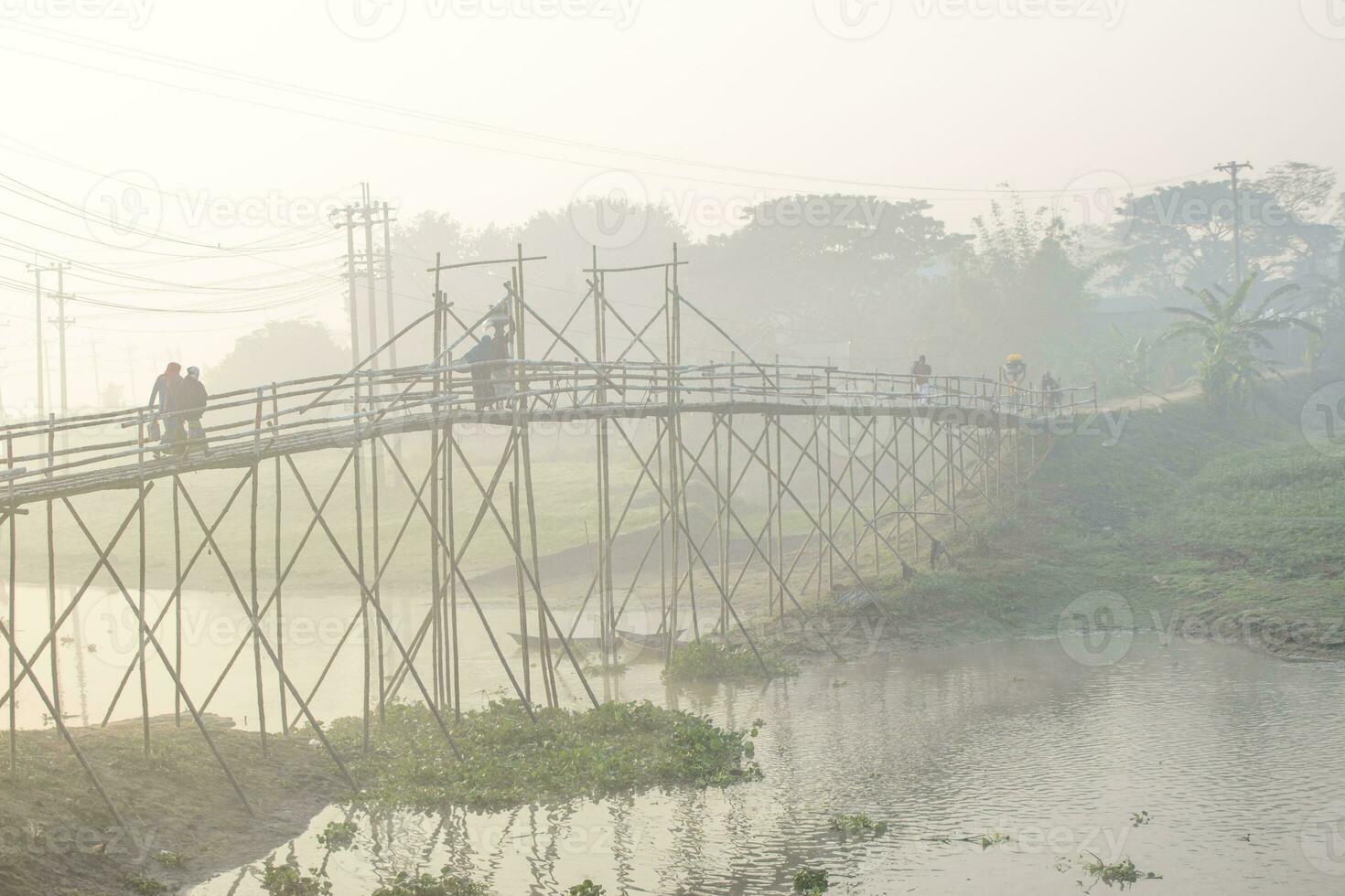 Villagers crossing on the traditional bamboo bridge on a foggy morning in Bangladesh photo
