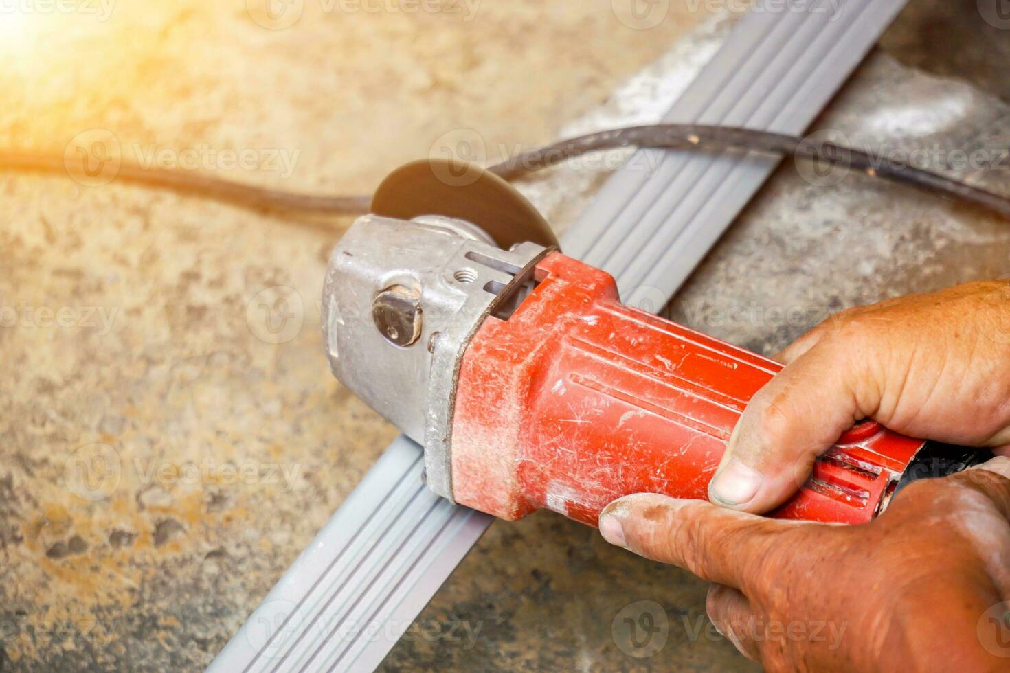 Closeup hands of laborer holding electric angle grinder working cutting aluminium lumber at construction site with sun flare background. photo
