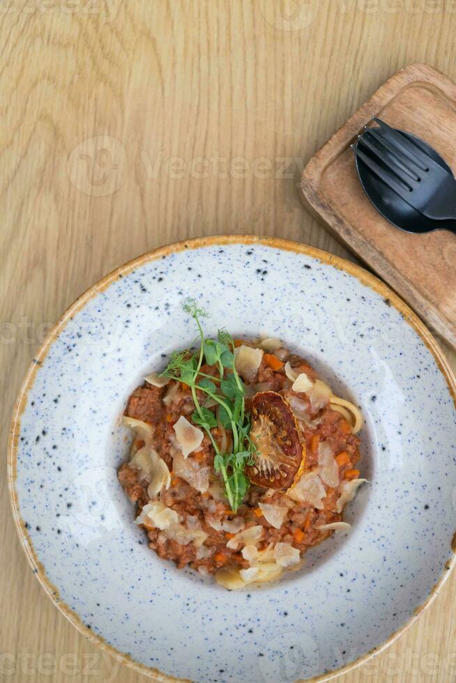 Bolognese in a bowl decorated dry tomato and microgreen on a wooden table top view, flat lay photo