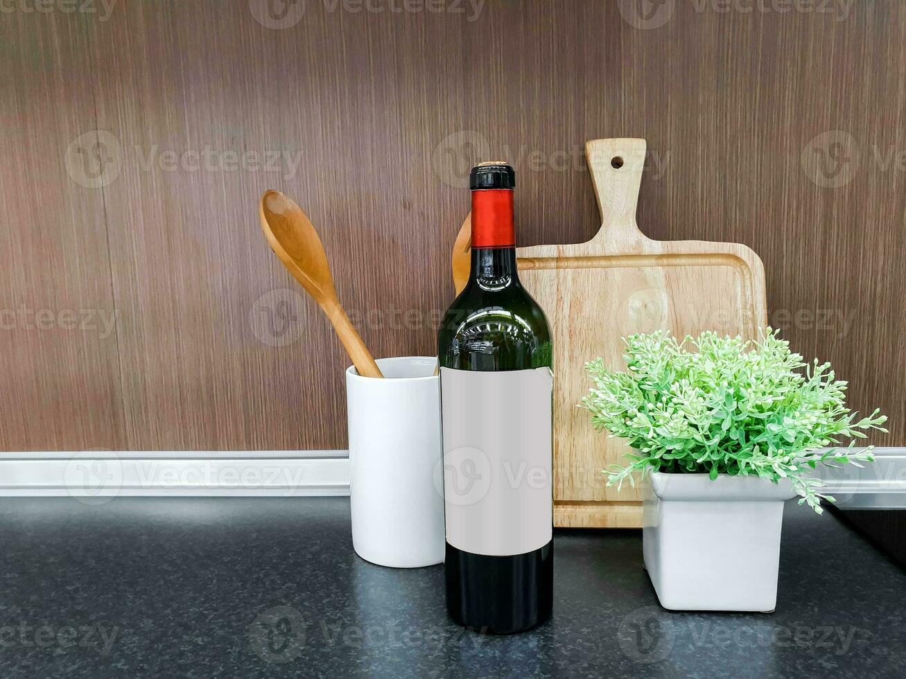 Wooden kitchenware and bottle of wine with decorate small green plant in white ceramic vase on kitchen shelves and wooden wall background. photo
