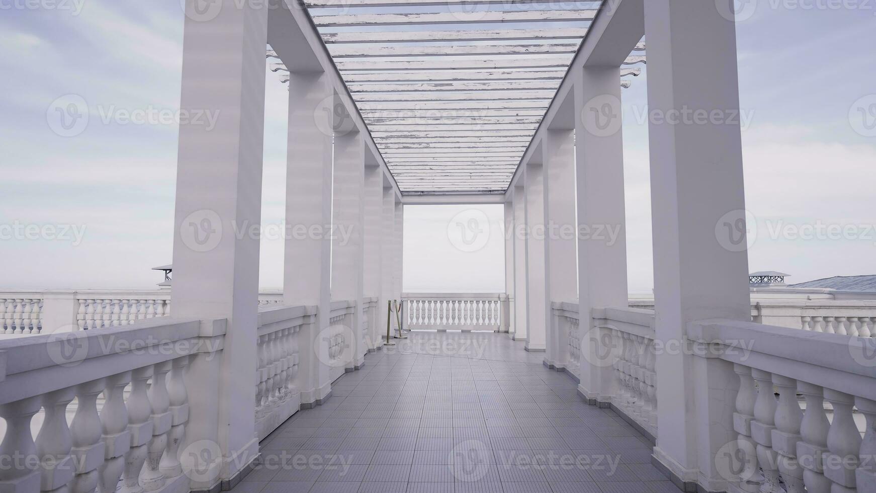 Walking among white marble pillars creating a beautiful corridor on blue sky background. Action. Marble beautiful pier on a summer day. photo