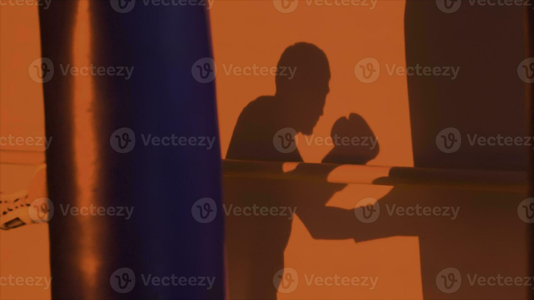 Silhouette or shadow of a boxer punching a punching bag close up, red light background. Silhouette of young male boxer hitting punching bag on red background. Man athlete standing and boxing. photo