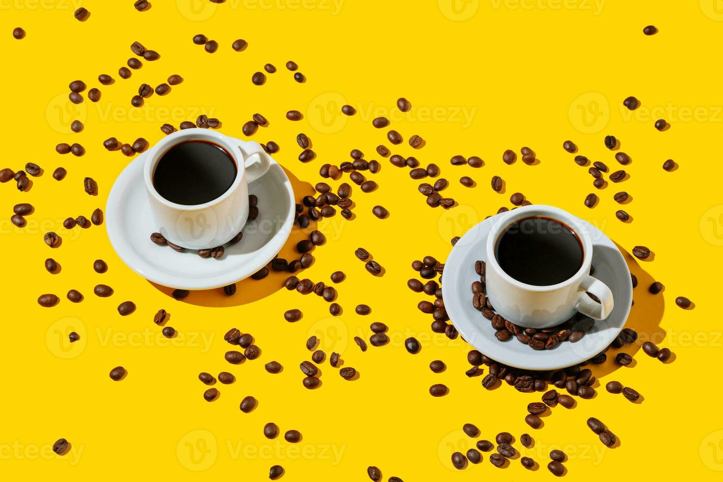 Two coffee cup over a bright yellow color background and many beans spilled around. photo