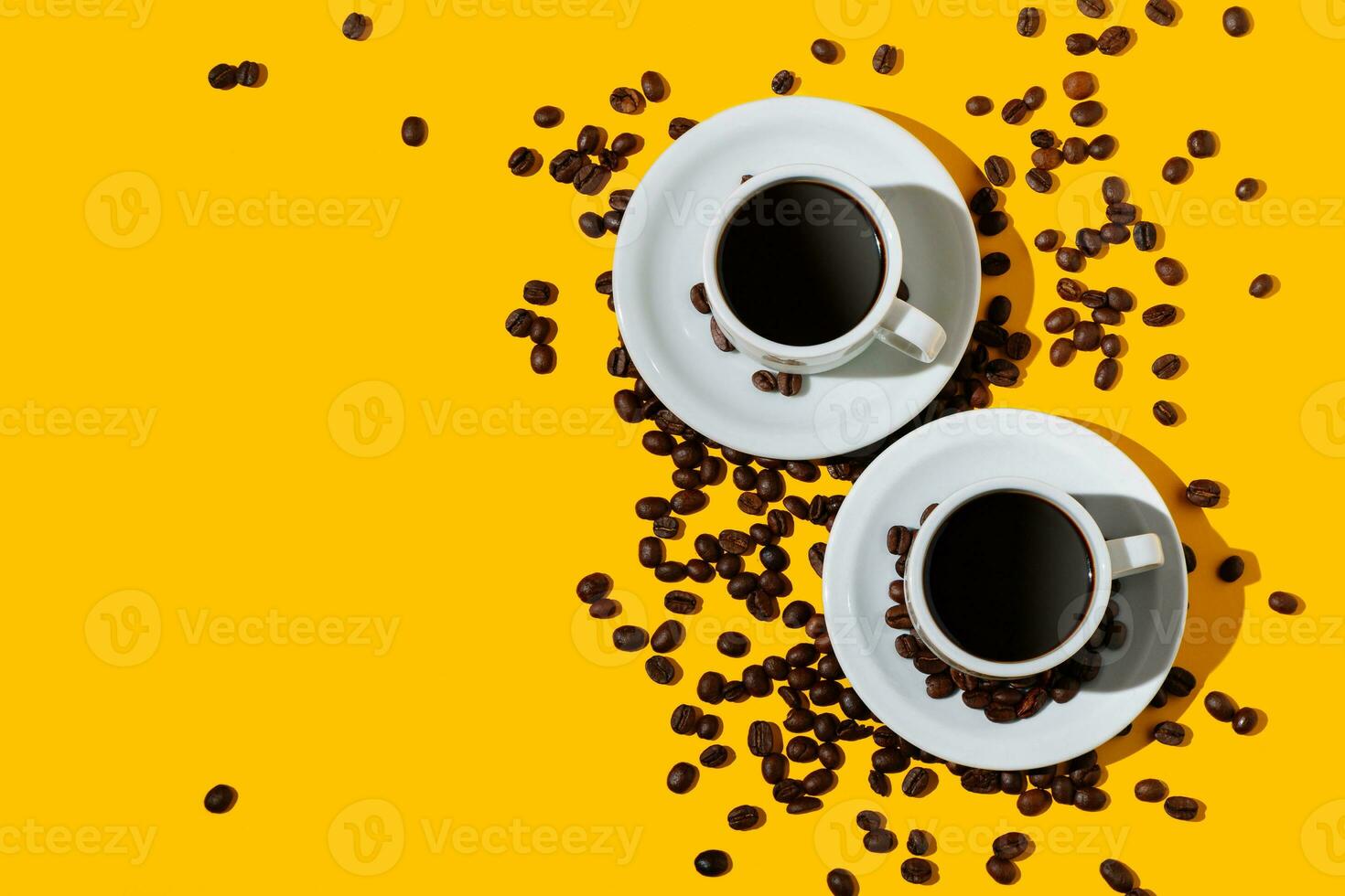 Top view of two coffee cup over a bright yellow color background and many beans spilled around. photo