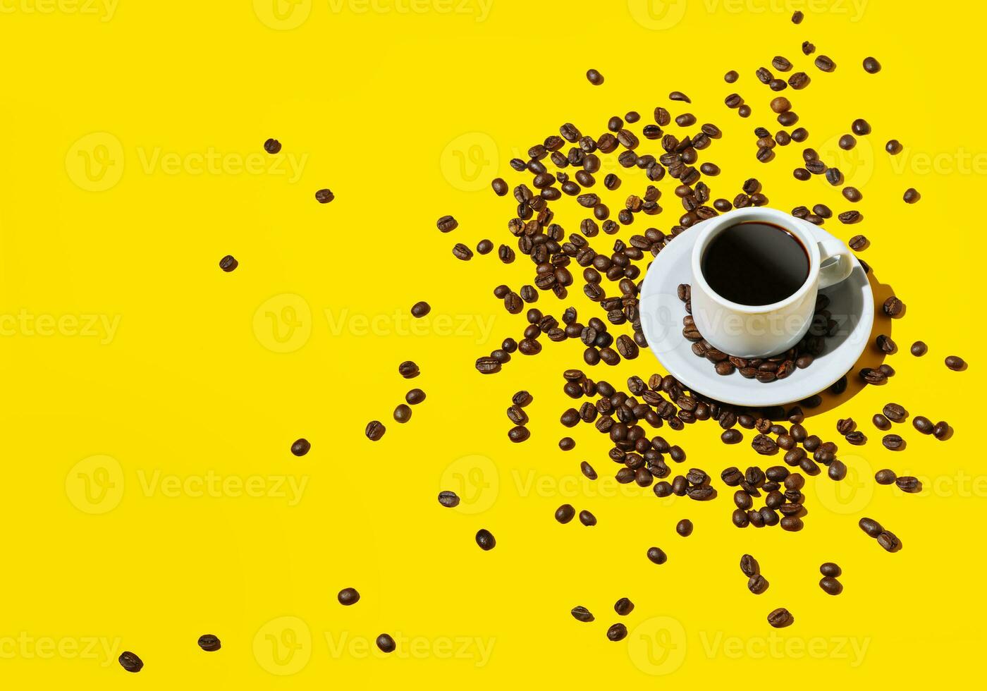 Coffee cup over bright yellow color background and many beans spilled around it. photo