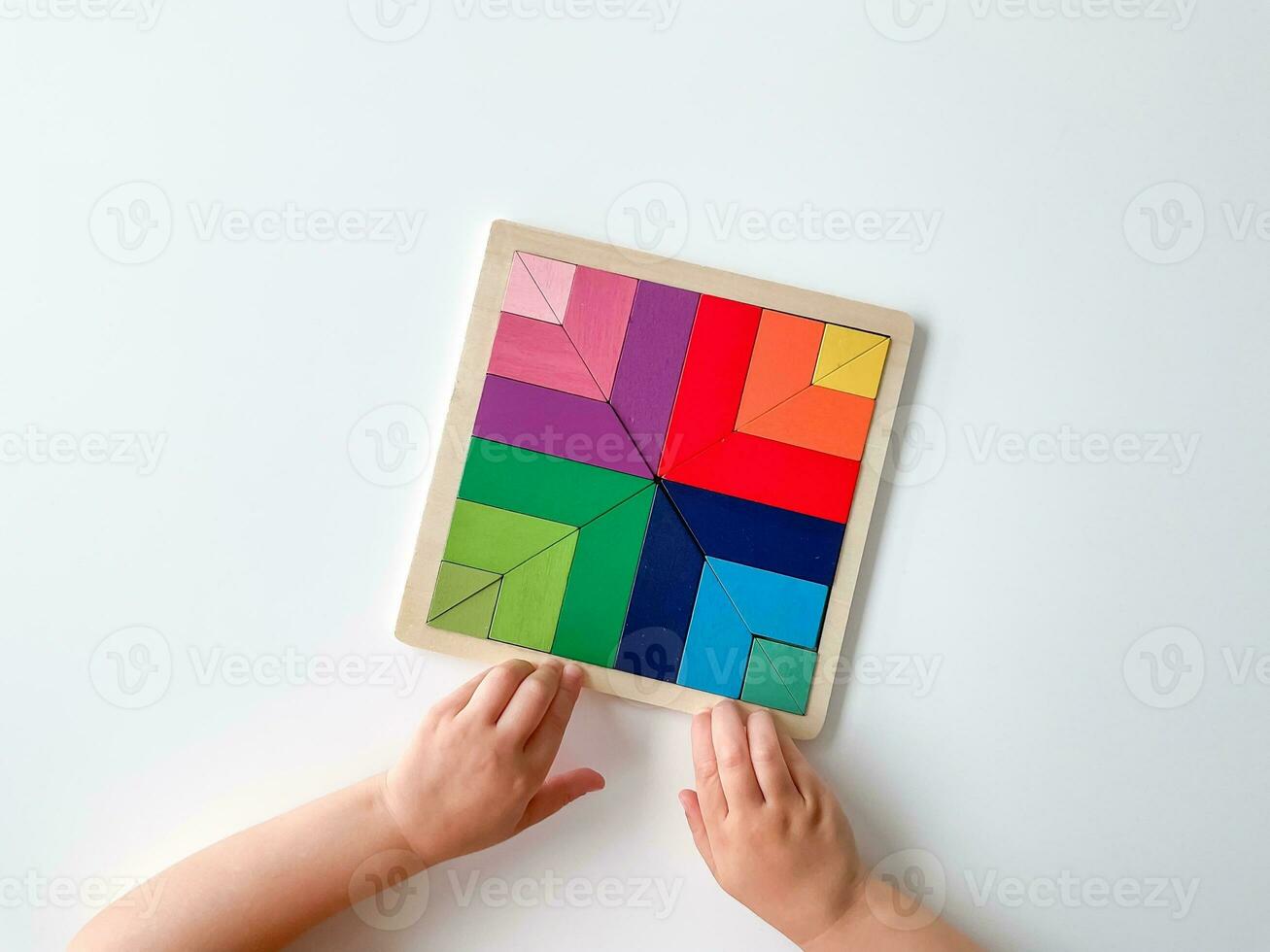 childs hand collects multicolored wooden mosaic on white background. photo