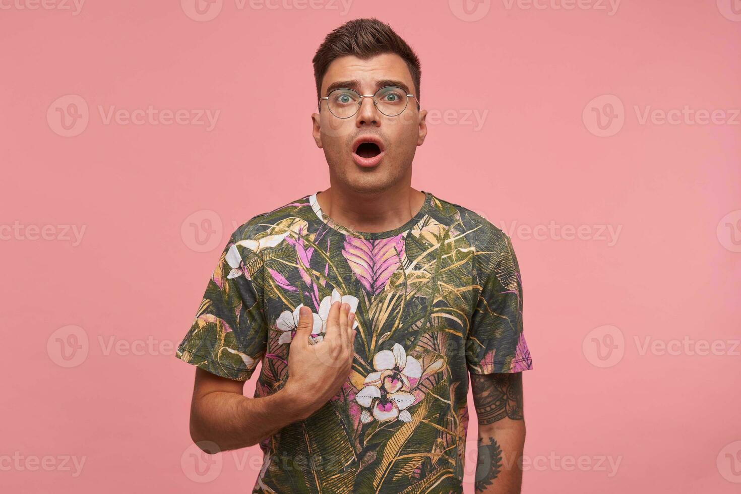 Portrait of attractive guy with dezad face, wearing glasses and flowered t-shirt, proving he is right, arguing, showing himself, isolate over pink background photo