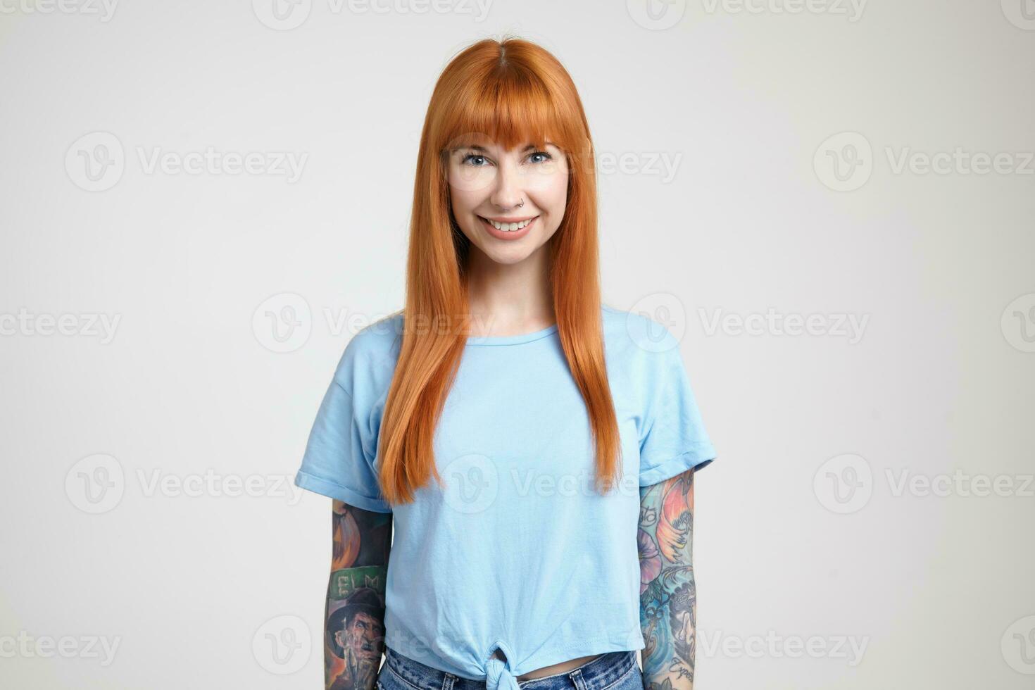 Indoor shot of young beautiful long haired woman with loose foxy hair smiling happily while looking gladly at camera, isolated over white background in casual wear photo