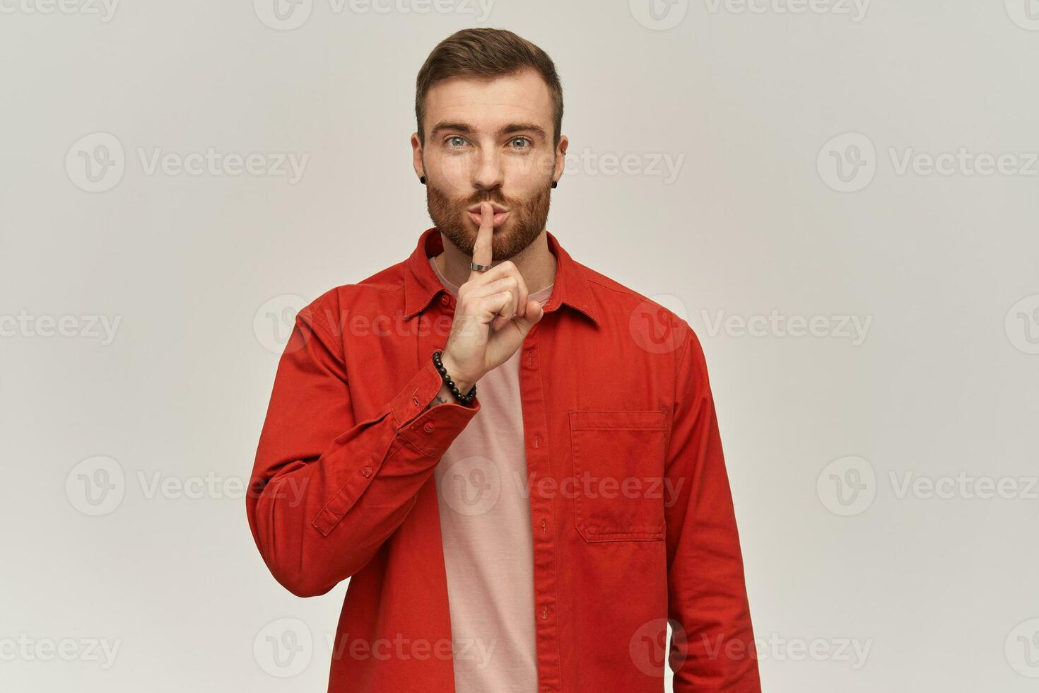 contento atractivo joven barbado hombre en rojo camisa demostración silencio gesto y mirando a cámara terminado blanco antecedentes foto
