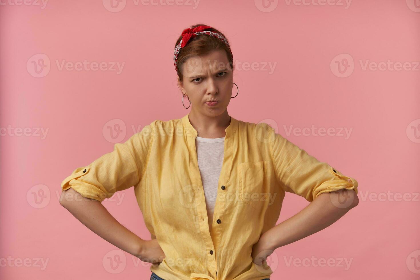 Portrait european brown haired woman 20s with natural makeup wearing stylish yellow shirt and red bandana posing against pink background emotion annoyed bored irritation looking at you hands on hips photo