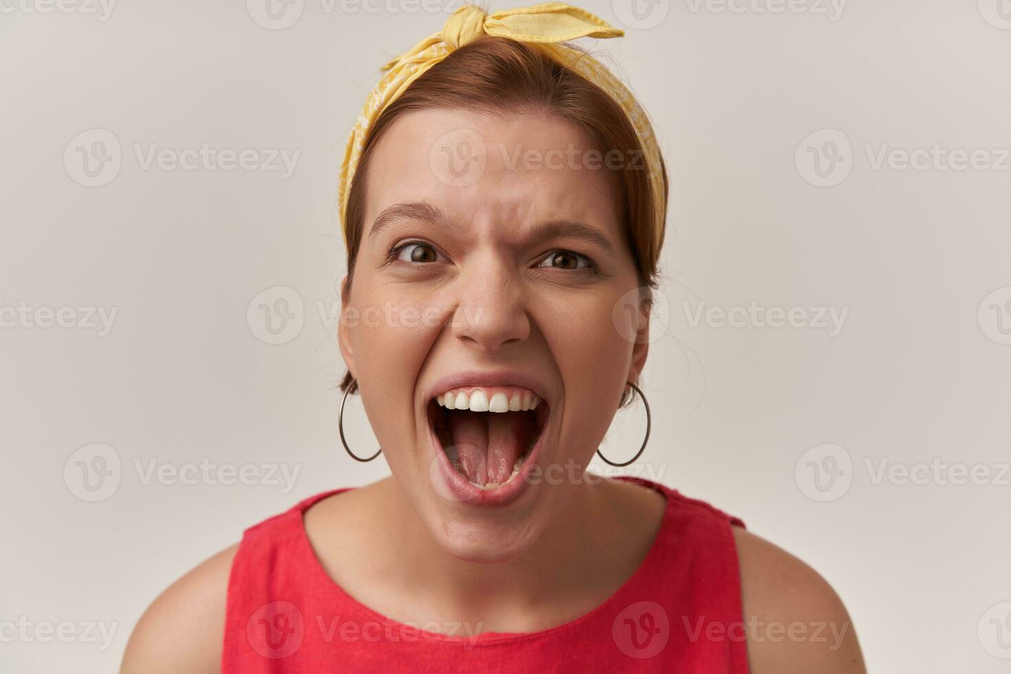 Image of screaming at you european young woman wearing fashionable red blouse and white bandana and ear rings with natural makeup posing against white wall emotion silly shout out loud insane annoyed photo