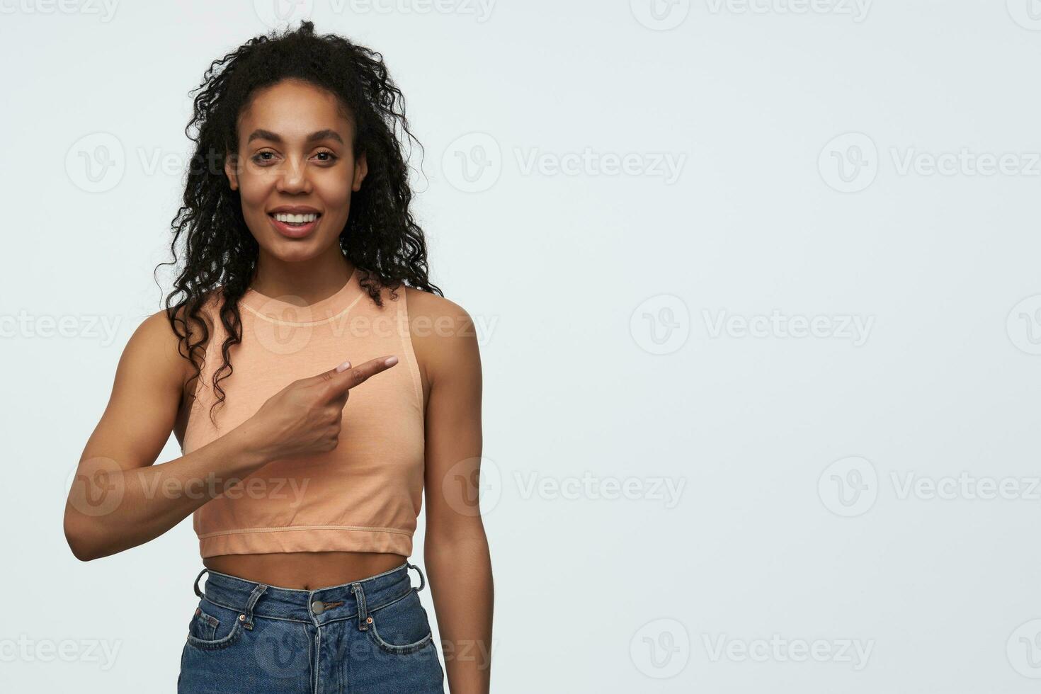 Happy beautiful african american young woman standing and pointing away to the side at copyspace isolated over white background photo