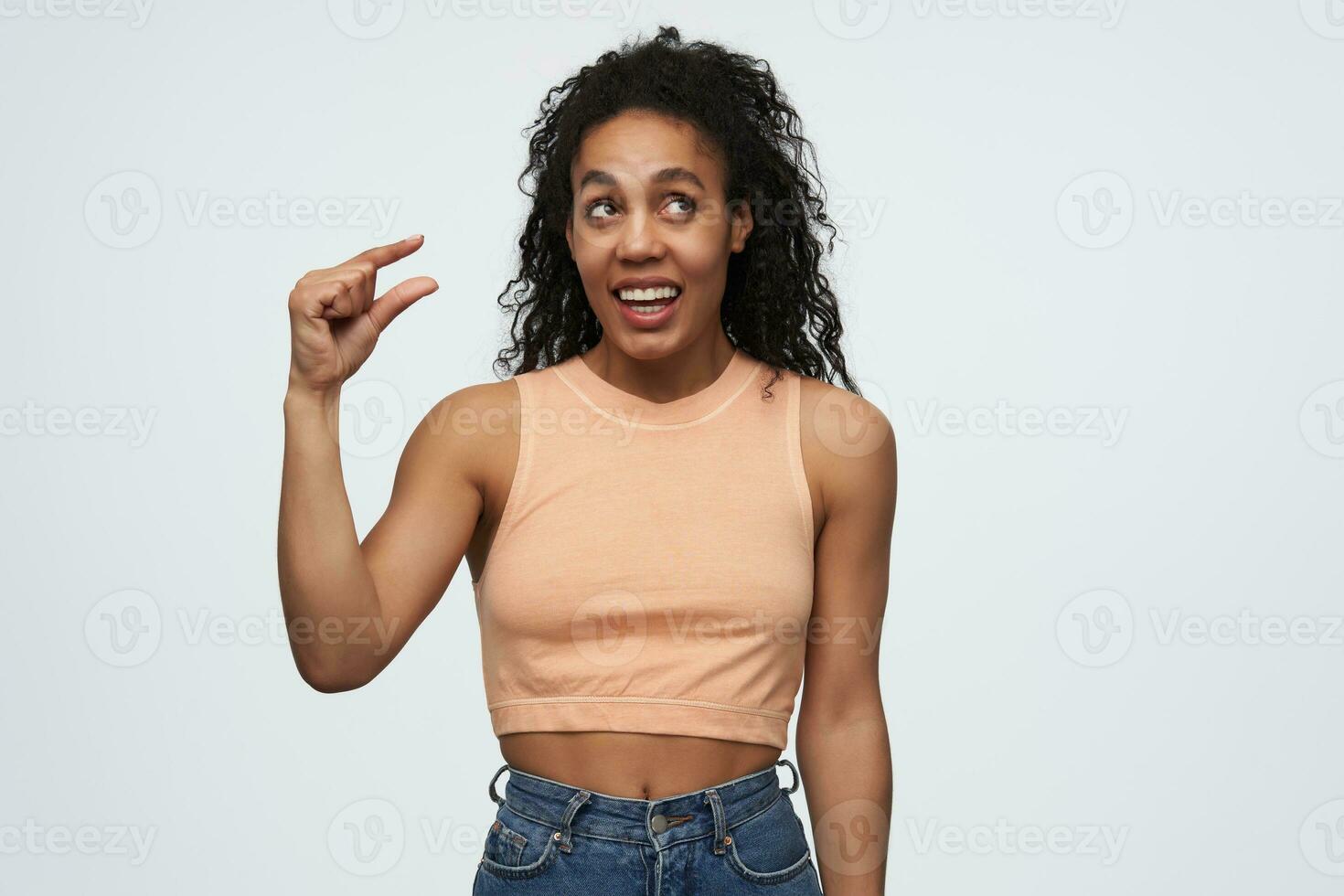 Smiling pensive african american young woman showing very small size by fingers isolated over white background photo