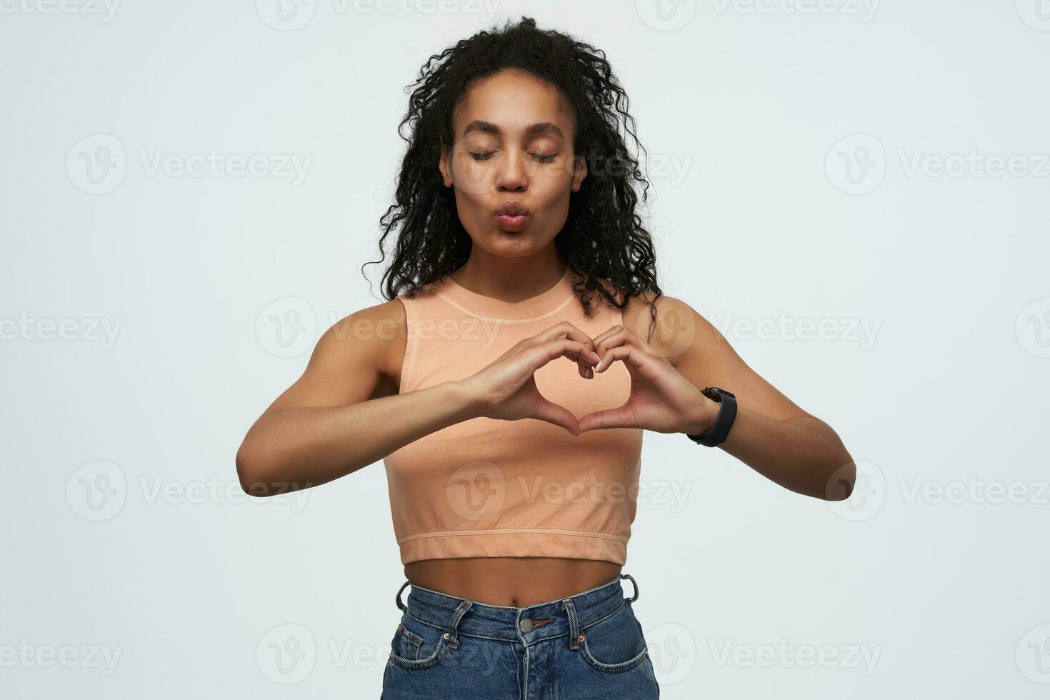 contento atractivo africano americano joven mujer con ojos cerrado demostración corazón forma por dedos y enviando Beso aislado terminado blanco antecedentes foto