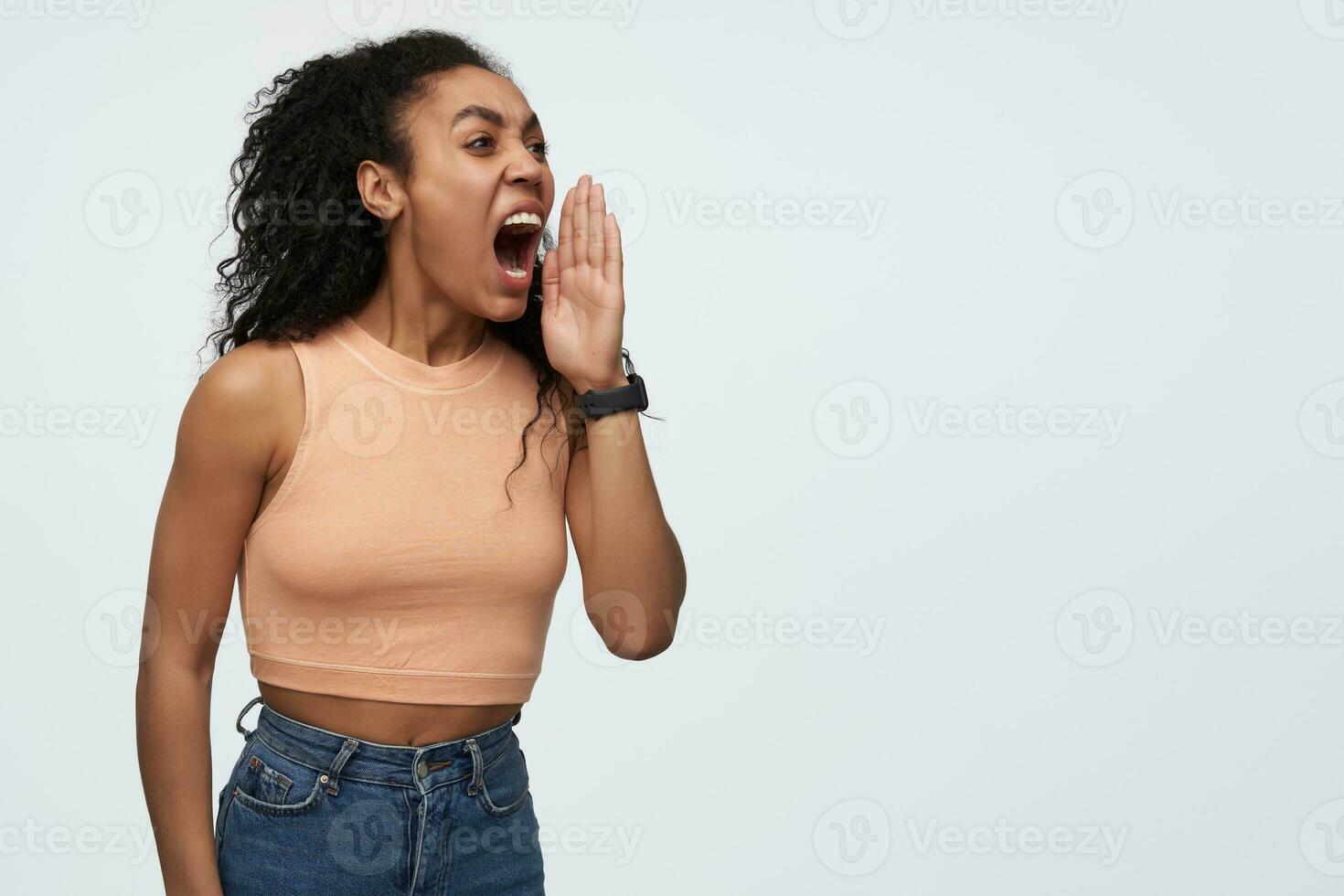 Mad furious african american young woman keeps hand near face and screaming loudly far away isolated over white background photo