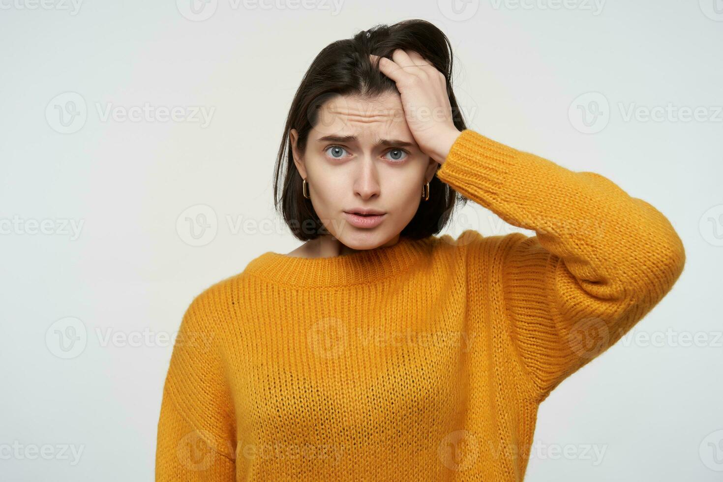 Indoor portrait of young brunette student female, feels confused and stressed, keeps her mouth widely opened with shocked facial expression, isolated over white background photo