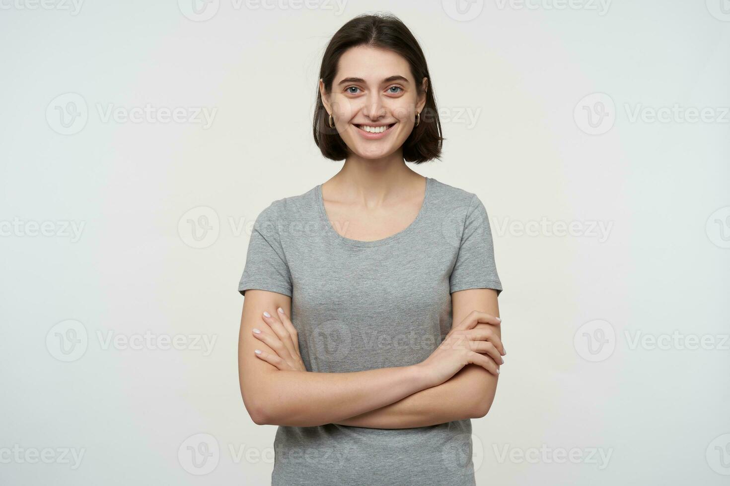 young brunette female student, looks directly into camera with brad smile on her face. Keeps her hands crossed. Isolated over white background photo