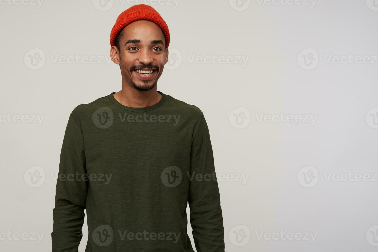 Charming young brown-eyed bearded brunette male with dark skin looking positively aside and smiling broadly, being in nice mood while posing over white background photo