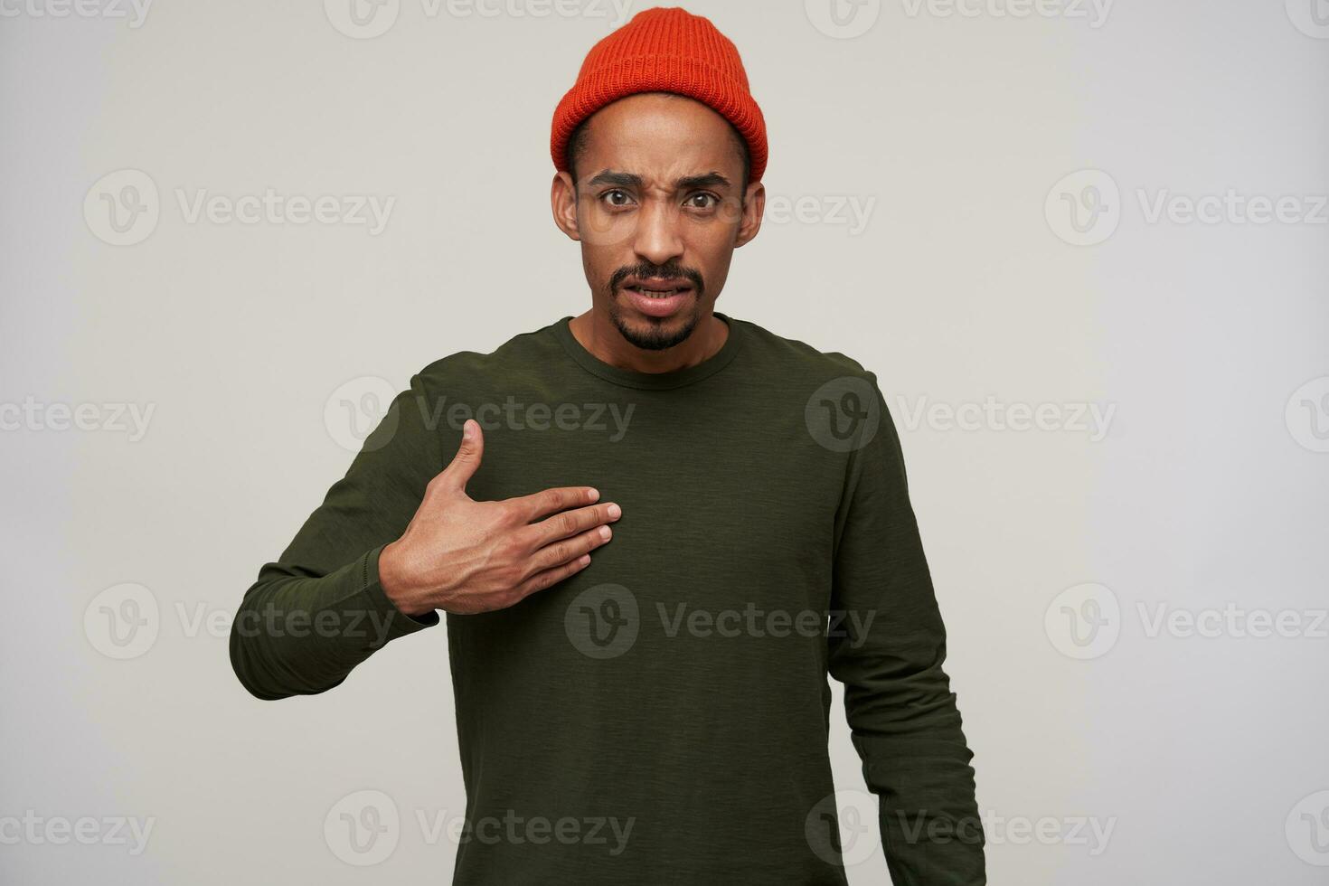 Studio shot of young irritated dark skinned brunette male with beard raising palm emotionally and frowning eyebrows while looking at camera, standing against white background photo