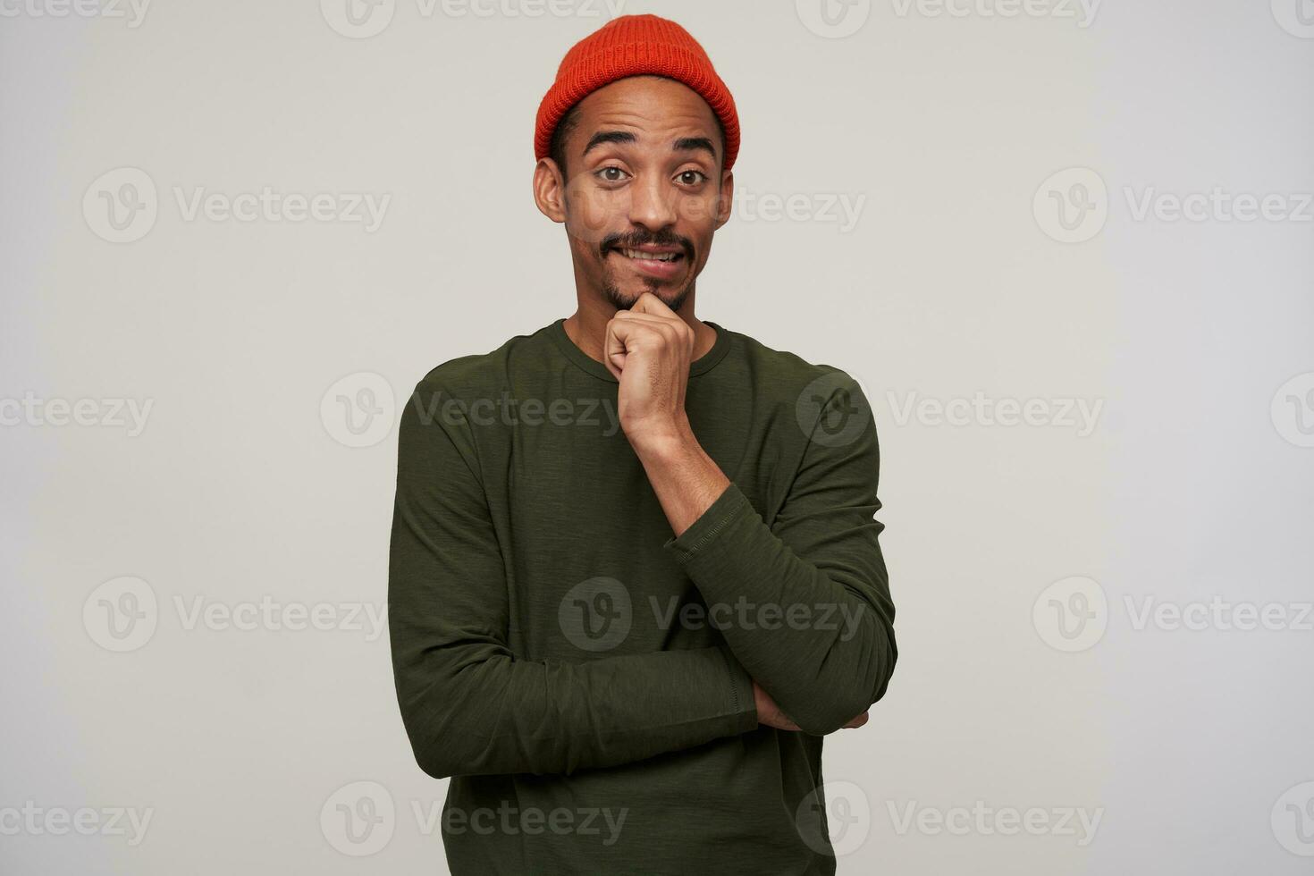 Portrait of confused young brown-eyed dark skinned brunette guy with beard biting underlip while looking at camera, wrinkling foehead while posing over white background photo