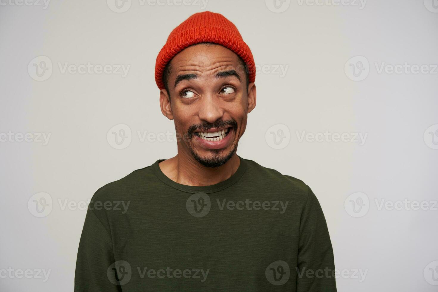 Cheerful young lovely dark skinned brunette man with beard showing his white perfect teeth while grimacing to camera, posing over white background in casual wear photo