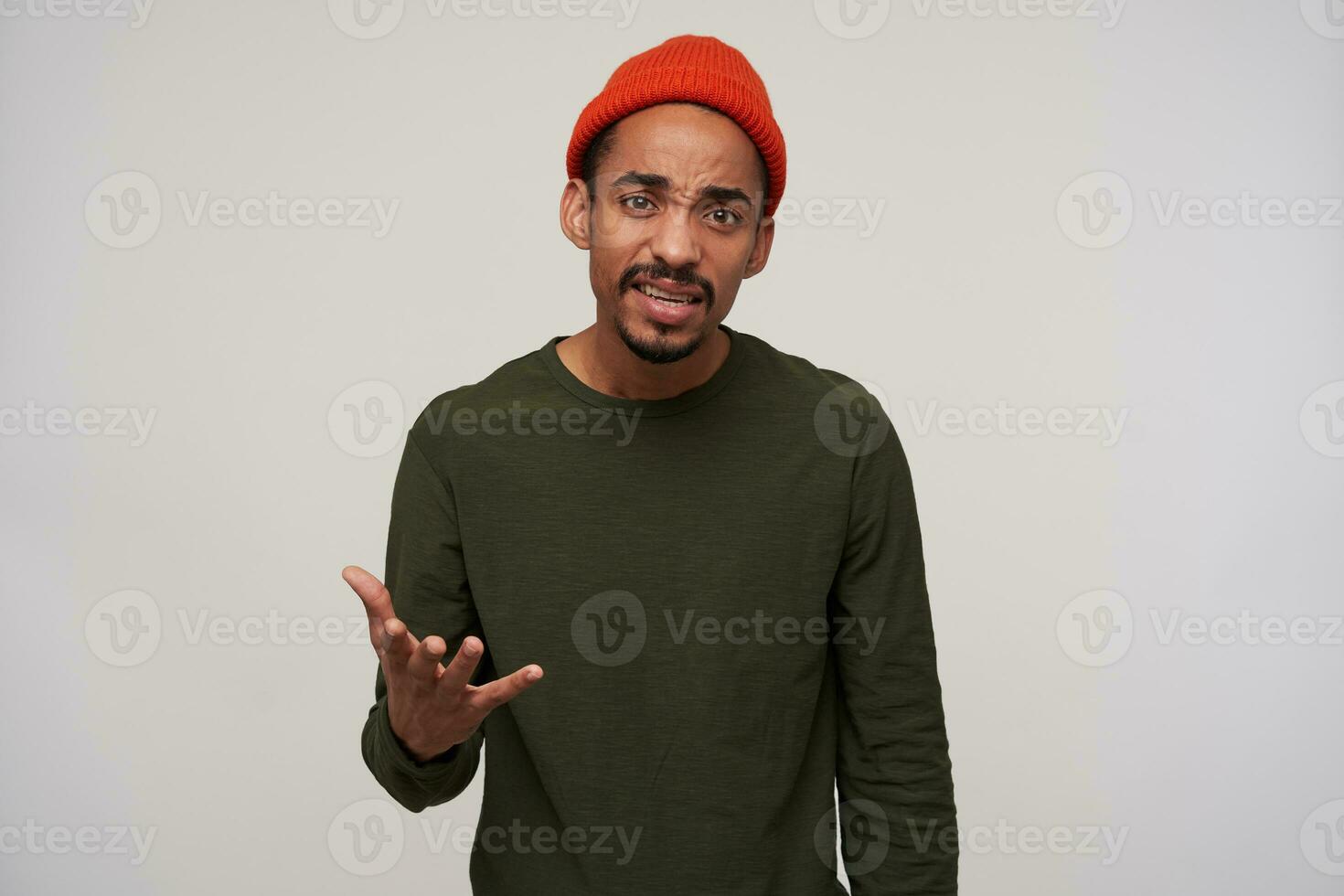 Studio shor of indignant young pretty dark haired bearded dark skinned guy looking confusedly at camera with raised palm, standing against white background photo